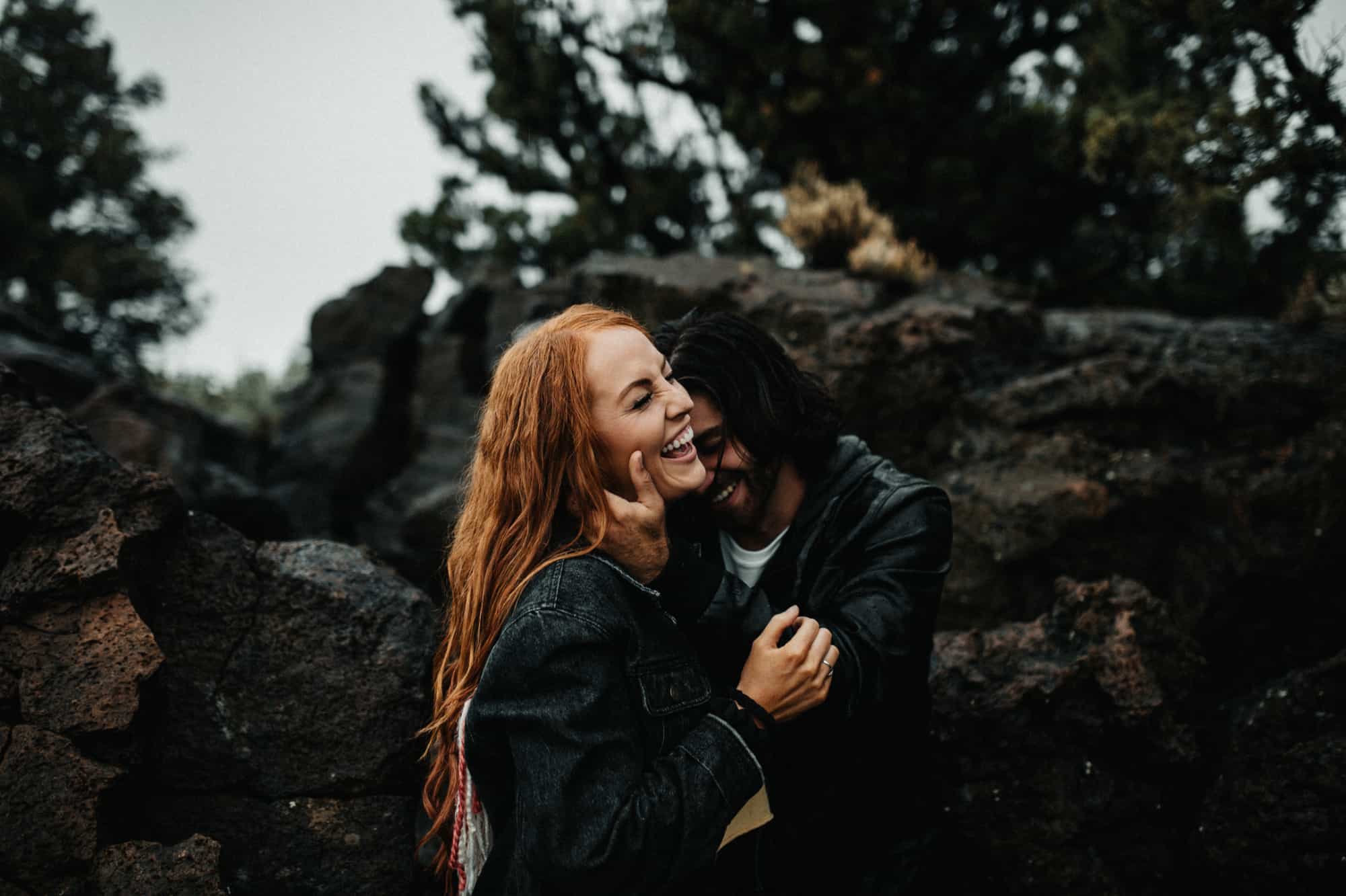joyful couple cuddling amongst dark oregon desert rocks